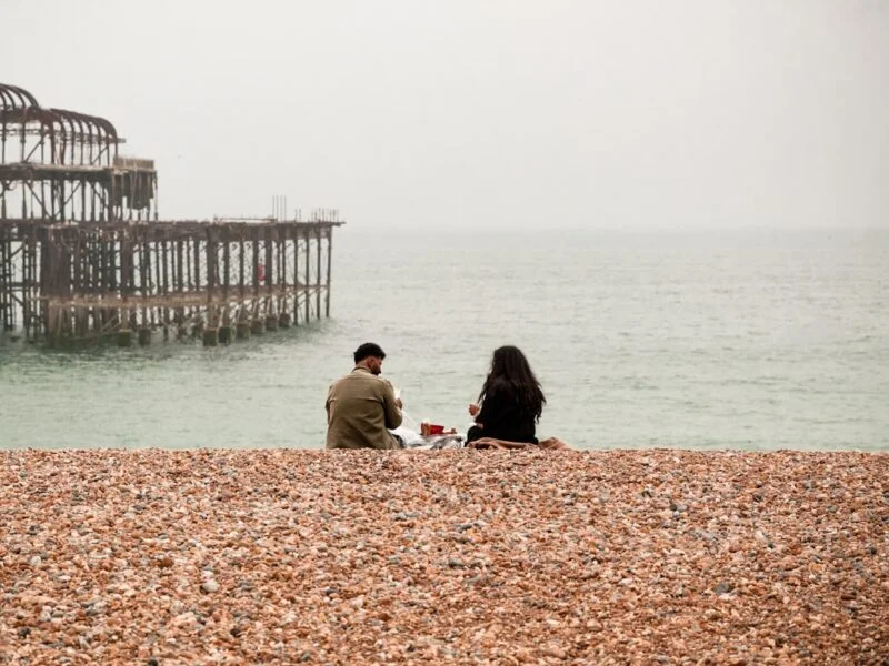 A person checking a mobile website on their phone while walking along Brighton seafront near the pier