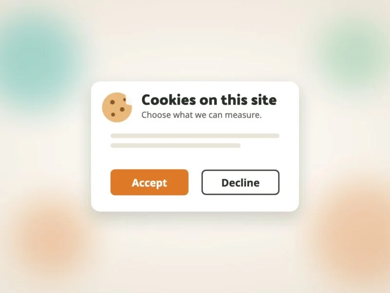 A cookie banner card with a small cookie icon, the heading "Cookies on this site", an orange Accept button and an outlined Decline button, over a soft blurred cream background.